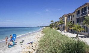 Une plage bordée d’une rangée de bâtiments, avec un ciel dégagé et une mer calme.