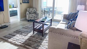 Un salon comprenant un canapé, un fauteuil et une table basse. Il y a un balcon avec du mobilier d’extérieur.