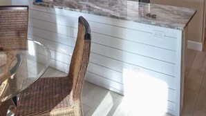 Une cuisine moderne avec des meubles blancs, un plan de travail en marbre et un coin repas doté de chaises en osier.