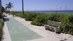 Une promenade en bord de mer avec un terrain de jeu de «shuffleboard», un banc et des palmiers.