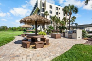 A patio area with a thatched umbrella, wooden benches, and a grill station. - Gulf and Bay Club- A203-Excellent Views (Siesta Key)