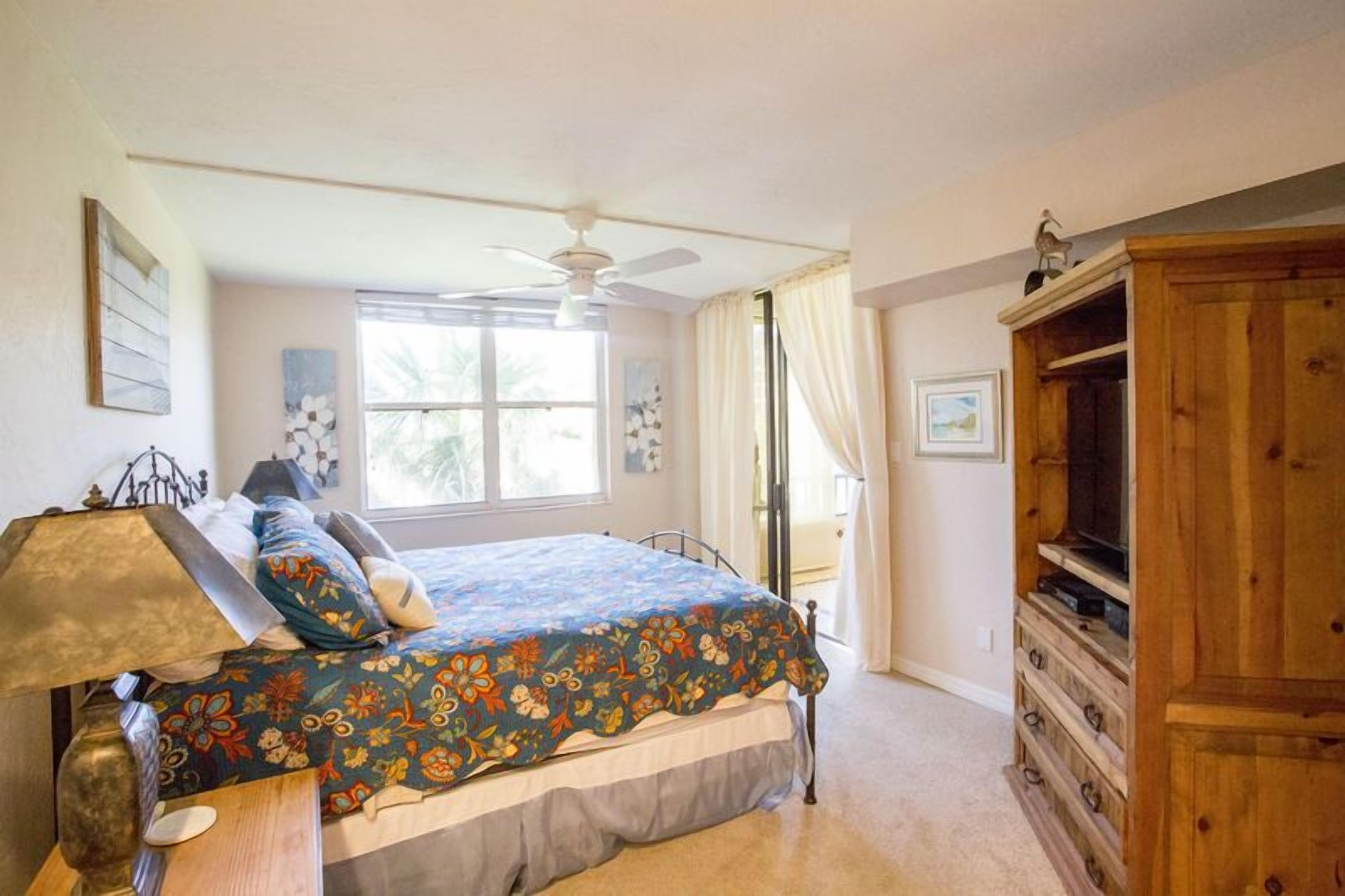 A bedroom with a bed, a ceiling fan, a wooden cabinet, and a window with curtains.