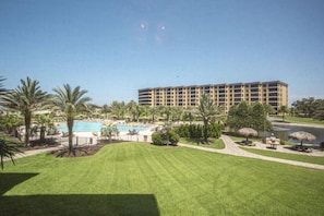 A hotel with a swimming pool, palm trees, and a well-maintained lawn.