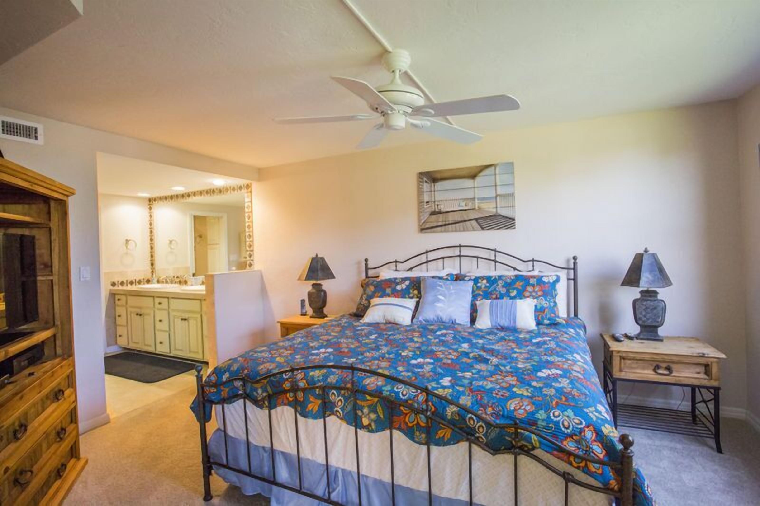 A bedroom with a bed, bedside tables, a ceiling fan, a mirror, and a wooden dresser.