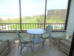 A balcony with a table and chairs, overlooking a golf course and a building.