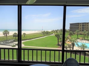 A view from a balcony overlooking a beach, a golf course, and a hotel building.
