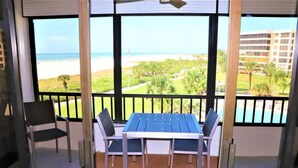 Een balkon met een tafel en stoelen, met uitzicht op een strand en een golfbaan.
