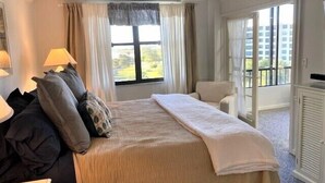 A hotel room with a bed, a chair, a desk, and a window with curtains.