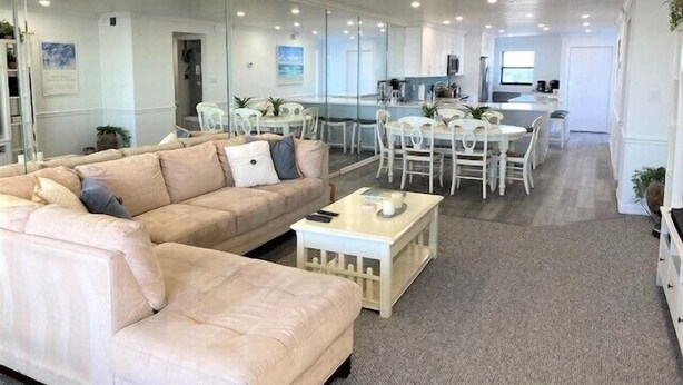 A spacious living area with a large sofa, a dining table with chairs, and a kitchen area in the background.