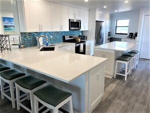 Une cuisine moderne avec des meubles blancs, un grand îlot central doté de tabourets, un réfrigérateur en acier inoxydable et un pare-feu bleu.