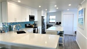 A modern kitchen with white cabinets, a central island with bar stools, a microwave, and a refrigerator.