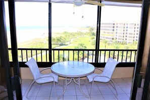 Un balcon doté d’une table ronde et de deux chaises, donnant sur un espace aménagé avec vue sur un bâtiment et une étendue d’eau.