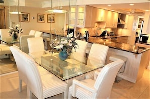 A modern kitchen with a central island, white upholstered chairs, and a glass dining table.