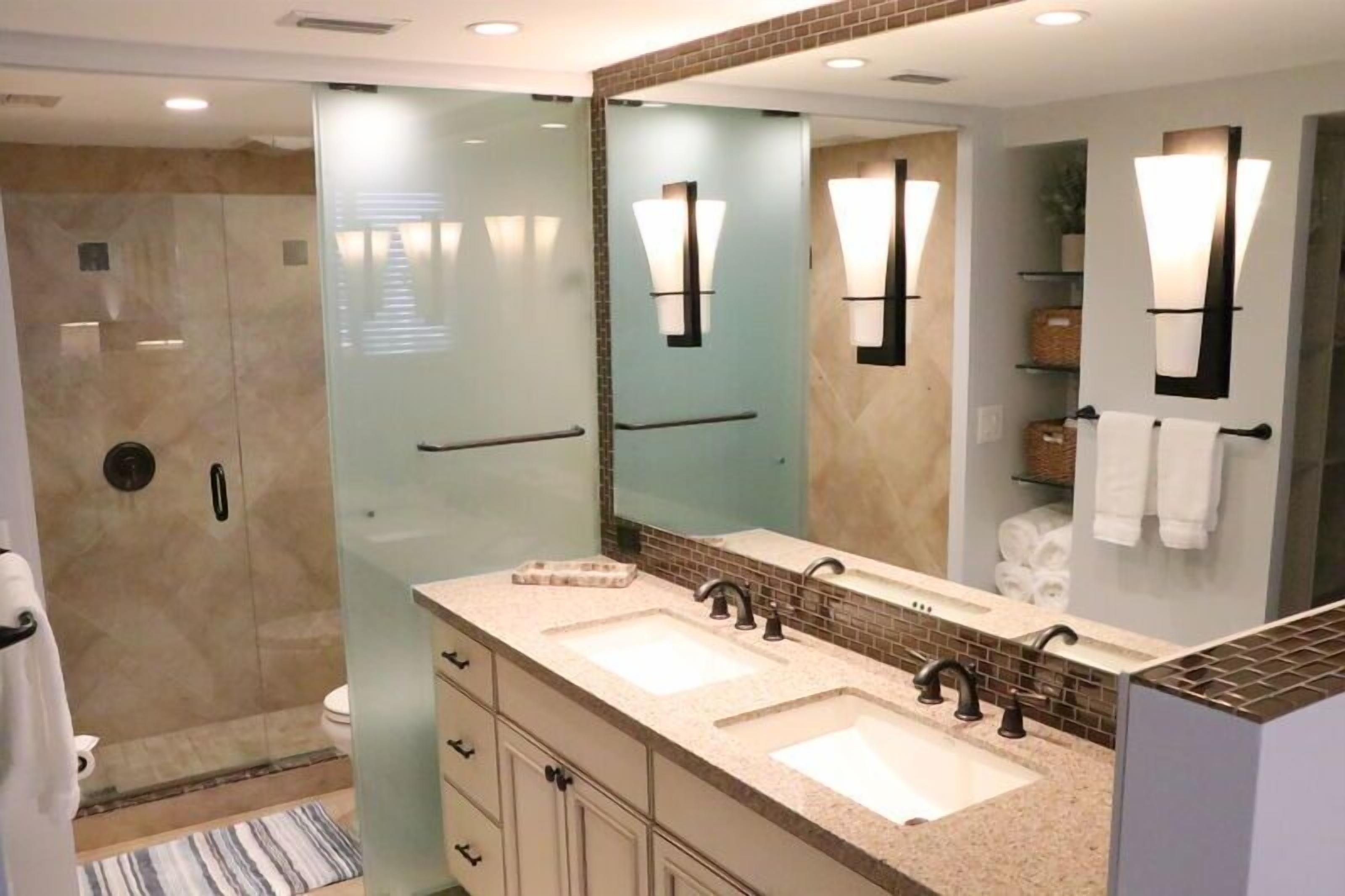 Une salle de bain moderne avec deux lavabos, une douche à parois de verre et un grand miroir.