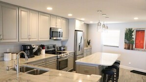 A modern kitchen with stainless steel appliances, a marble countertop, and a central island with bar stools.