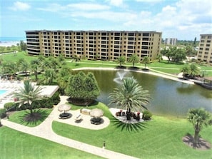 A hotel with a large building, a swimming pool, and a landscaped area with palm trees and a pond.