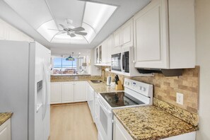 Une cuisine moderne avec des armoires blanches, des comptoirs en granit, un four encastré et un ventilateur de plafond.