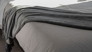 Una cama con ropa de cama blanca y una manta gris.