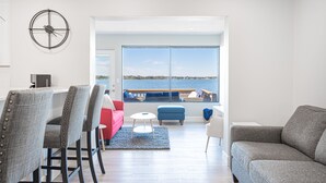 Una sala de estar moderna con vista a un cuerpo de agua, un comedor con sillas, un sofá rojo y un sofá gris.