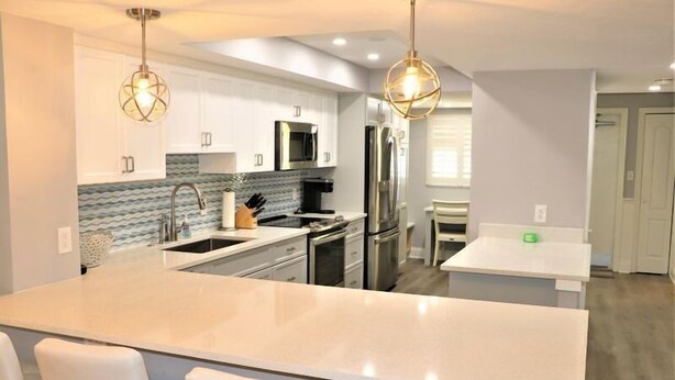 A modern kitchen with white cabinets, stainless steel appliances, and a central island with seating. - Gulf and Bay Club- B205 (Siesta Key)