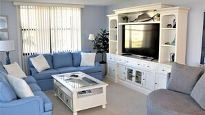 A living room with a blue sofa, a white coffee table, and a TV on a white cabinet. - Gulf and Bay Club- B205 (Siesta Key)