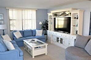 Een woonkamer met een blauwe bank, een witte salontafel en een televisie op een wit tv-meubel.
