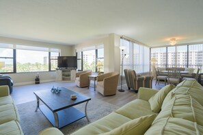 A spacious living room with a large window, a flat-screen TV, a coffee table, and comfortable seating. - Gulf and Bay Club- B301 Updated end unit! (Siesta Key)