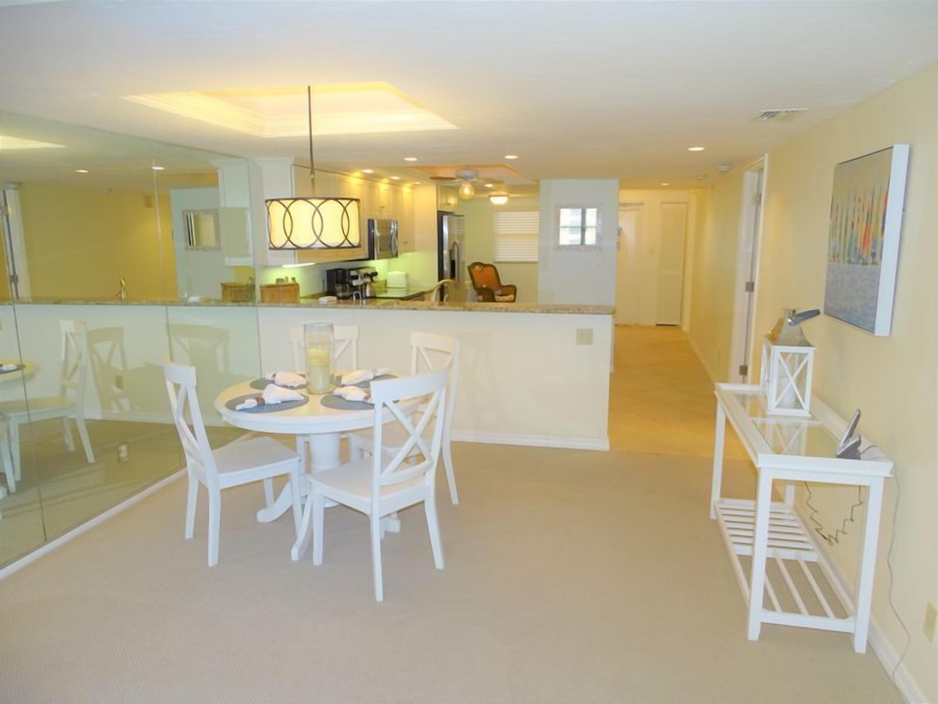 A modern kitchen with a central island, a dining area with white chairs, and a small white table.