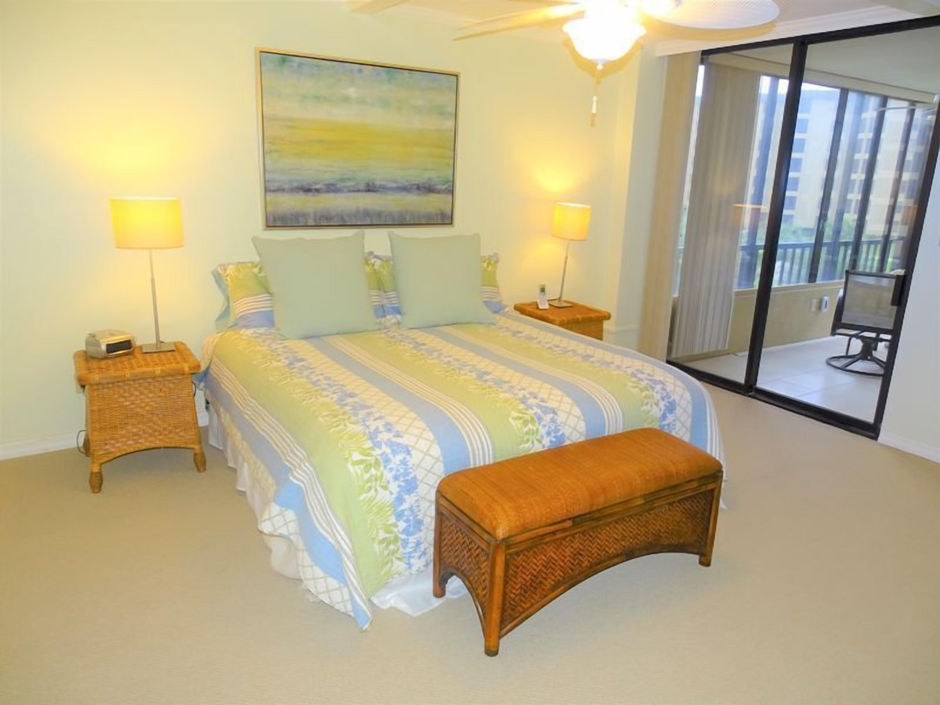 Ein Schlafzimmer mit einem Bett, zwei Nachttischen, einer Bank, einem Gemälde und einem Balkon.