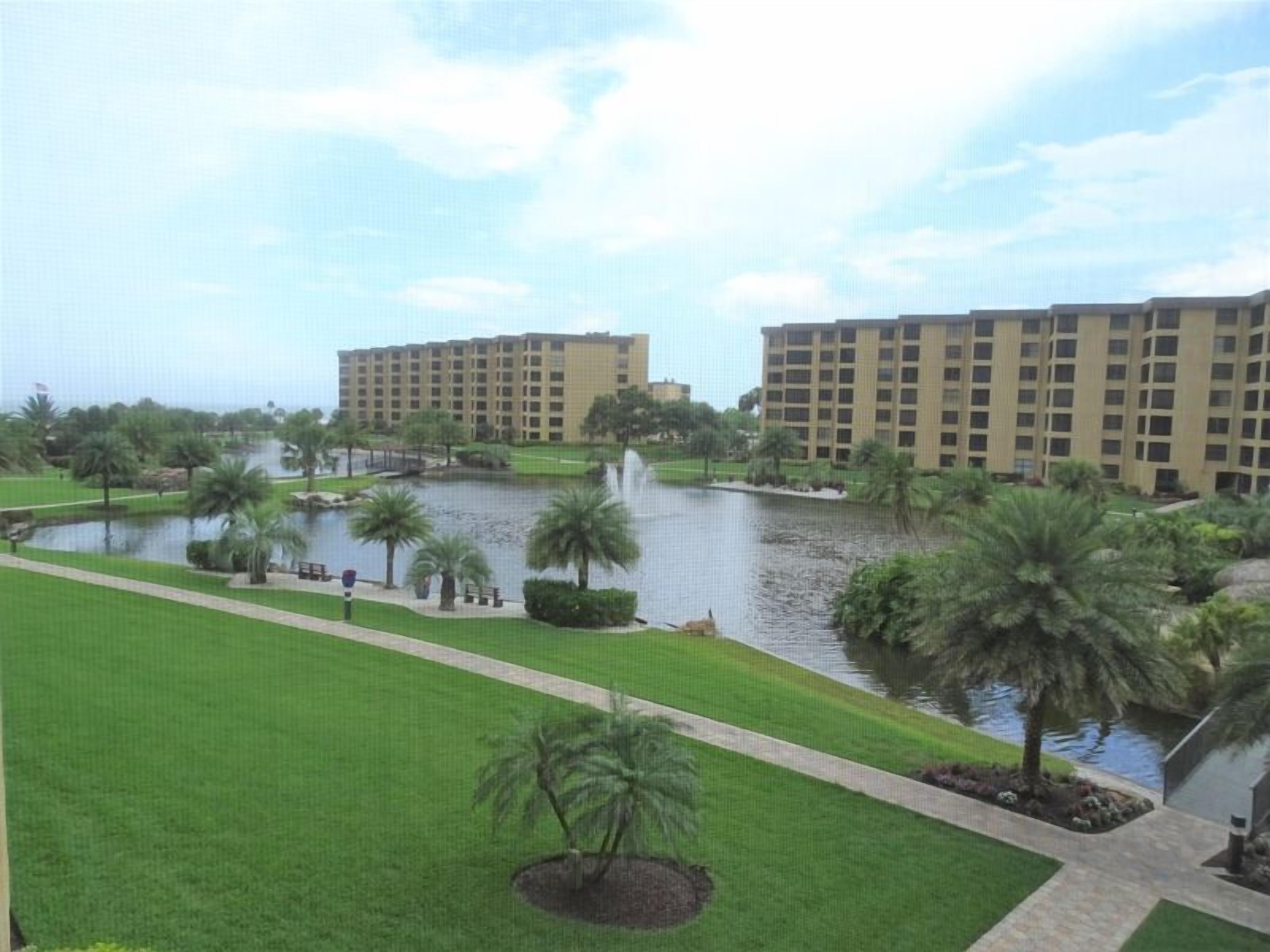 A hotel with a large water body in the foreground, surrounded by well-maintained lawns and palm trees.