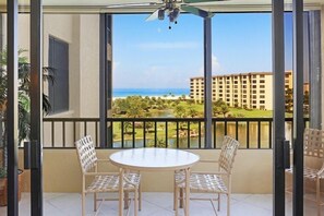 A balcony with a table and chairs, a view of a golf course, and a building in the background.