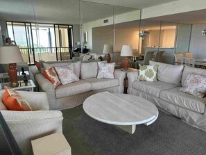 Un salon moderne avec un ensemble de canapés de couleur beige, une table basse ronde et une cloison en verre.