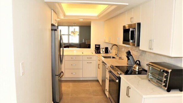 A modern kitchen with white cabinets, stainless steel appliances, and a marble countertop.