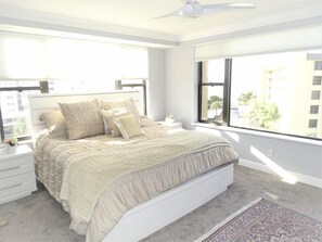 A bedroom with a bed, nightstands, a rug, and large windows.