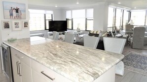 Una cocina moderna con encimera de mármol, armarios blancos y un televisor de pantalla plana.