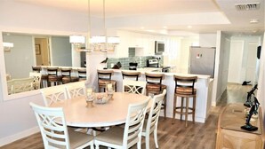 A modern kitchen with white cabinets, a central island, and a dining area with a round table and chairs. - Gulf and Bay Club- B707 (Siesta Key)