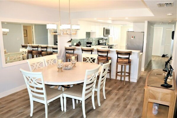A modern kitchen with white cabinets, a central island, and a dining area with a round table and chairs.