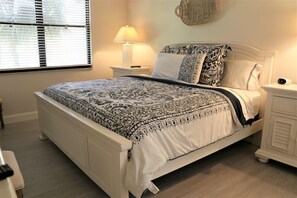 A neatly made bed with a patterned bedspread, a bedside lamp, and a nightstand with a lamp. - Gulf and Bay Club C105: Siesta Key Condo with Direct Pool and Beach Access! (Siesta Key)
