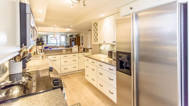 A modern kitchen with stainless steel appliances, white cabinetry, and a central island. - Gulf and Bay Club- C201 Beautiful updates! (Siesta Key)