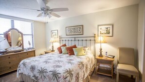A bedroom with a bed, two bedside tables, a chair, a ceiling fan, and wall art. - Gulf and Bay Club- C201 Beautiful updates! (Siesta Key)