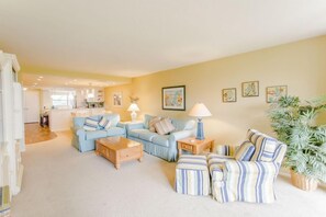 A spacious living room with a light blue sofa set, a striped armchair, and a coffee table. There are two lamps on side tables, and a potted plant in the corner. - Gulf and Bay Club- C202 Amazing kitchen! (Siesta Key)