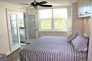 A bedroom with a bed, a ceiling fan, a window with a view of greenery, and a door leading to an outdoor area. - Gulf and Bay Club- C207 (Siesta Key)