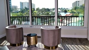 A room with large windows overlooking a pool and greenery, two modern chairs, and a small gold-colored side table. - Gulf and Bay Club- C207 (Siesta Key)