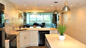 A modern kitchen with white cabinetry, a central island, pendant lighting, and a view of the outdoors. - Gulf and Bay Club- C207 (Siesta Key)