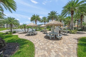 Relax in a serene outdoor space with a paved patio, umbrellas, and comfortable seating amidst lush greenery and a tranquil body of water.