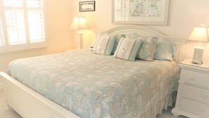 A bedroom with a bed, two bedside tables, and a window with shutters. - Gulf and Bay Club- C305 (Siesta Key)