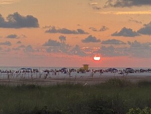 Escena de playa con atardecer, gente y sombrillas.