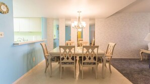 A dining area with a table and chairs, a chandelier, and a kitchen visible in the background.