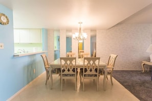 A dining area with a table and chairs, a chandelier, and a kitchen visible in the background.