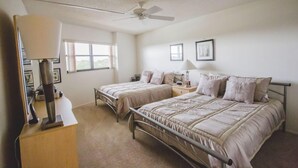 A bedroom with two single beds, a ceiling fan, a desk with a lamp, and a window. - Gulf and Bay Club- C503 Beautifully updated with great views! (Siesta Key)